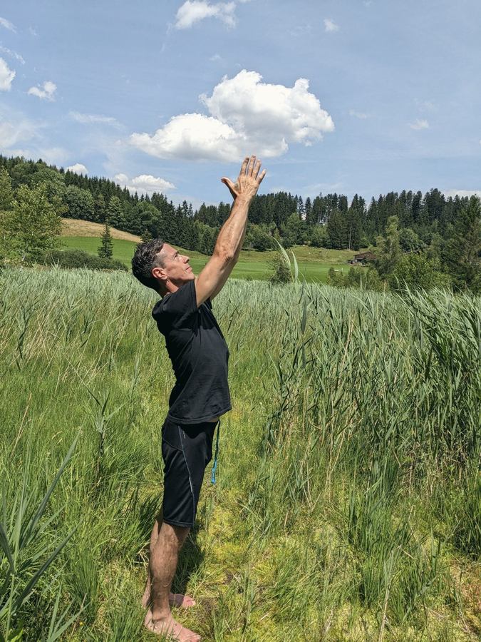 Gustavo standing in a meadow, arms reaching to the sky
